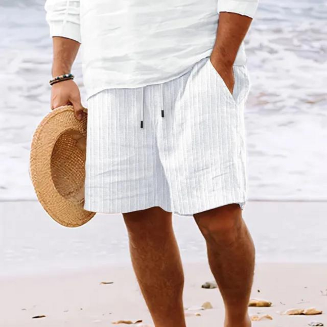 Un homme portant un short à rayures blanches et grises, avec poches et cordon de serrage, idéal pour un look décontracté et tendance à la plage.