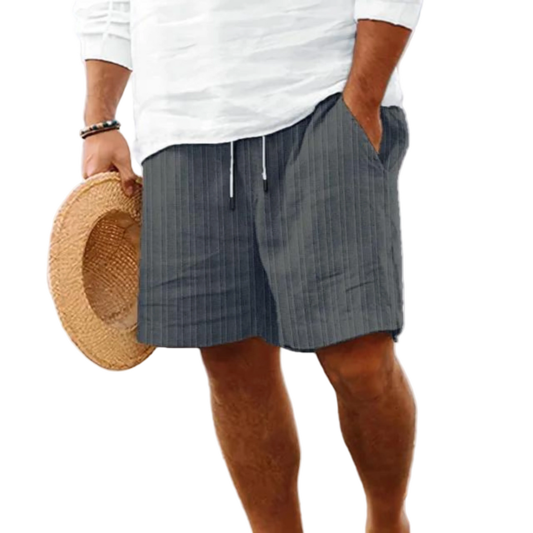 Un homme portant un short à rayures grises, avec poches et cordon de serrage, idéal pour un look décontracté et moderne à la plage.