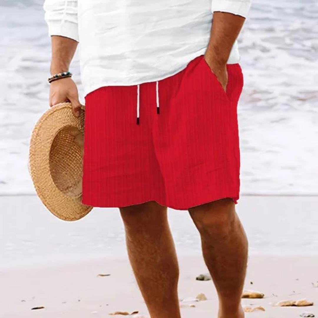 Un homme portant un short à rayures rouges avec poches et cordon de serrage, idéal pour un look décontracté et dynamique à la plage.