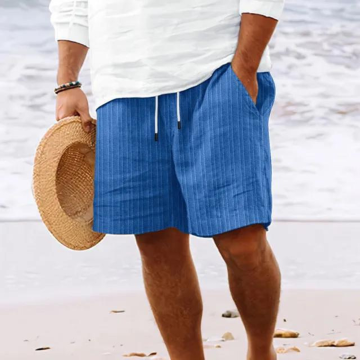 Un homme portant un short à rayures bleues avec poches et cordon de serrage, parfait pour un look décontracté et tendance à la plage.