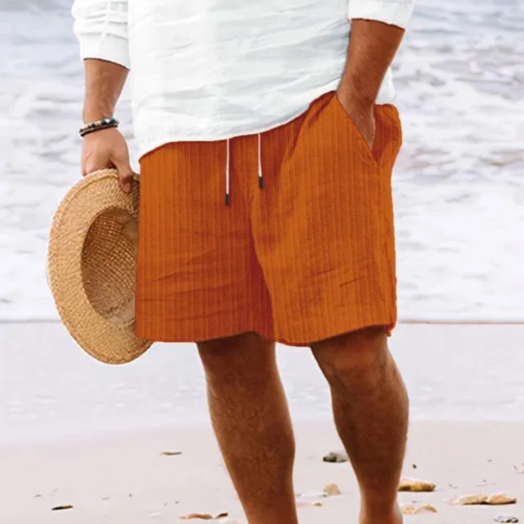 Un homme portant un short à rayures orange, avec poches et cordon de serrage, parfait pour un look décontracté et tendance à la plage.