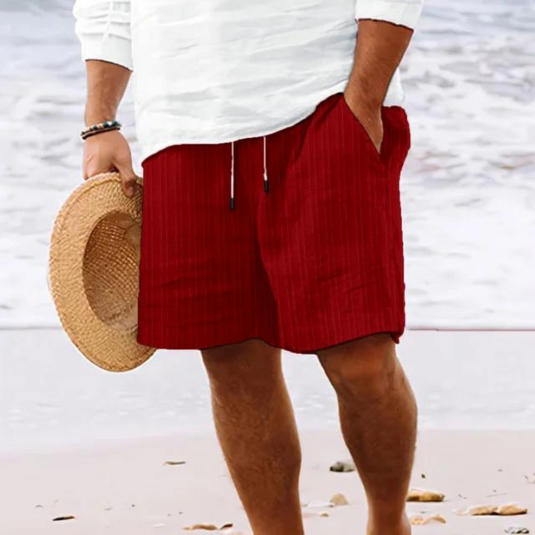 Un homme portant un short à rayures rouges avec poches et cordon de serrage, parfait pour un look décontracté et moderne à la plage.