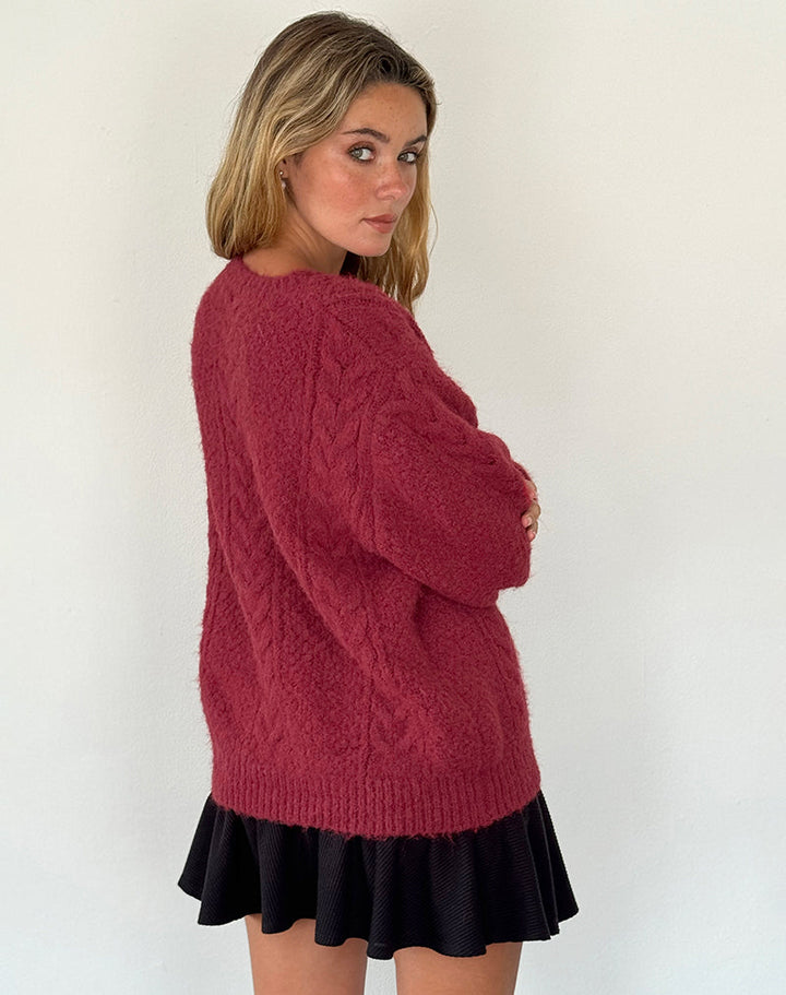 Femme vue de profil portant un cardigan bordeaux en maille épaisse avec un motif torsadé discret. Le vêtement présente une coupe ample et confortable, parfaite pour un style décontracté et tendance. Elle l’associe à une jupe noire courte fluide, créant un look chic et moderne idéal pour la saison automne-hiver.