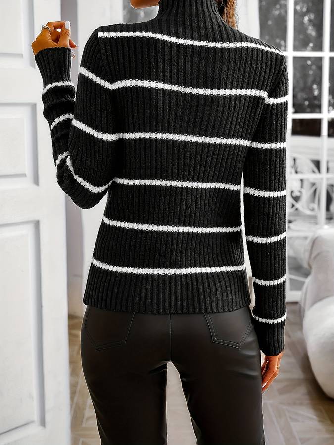 Vue de dos d’une femme portant un pull noir à col montant avec des rayures horizontales blanches. Le vêtement en maille côtelée est associé à un pantalon noir ajusté. La coupe près du corps et la texture du tissu soulignent un style moderne et raffiné, idéal pour la saison froide.