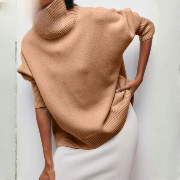 Women's oversized brown turtleneck sweater with short sleeves and a loose fit. The turtleneck is wide and ribbed, while the bottom of the sweater features a ribbed finish. Worn with a white skirt, this sweater creates a comfortable and elegant look, perfect for winter days.