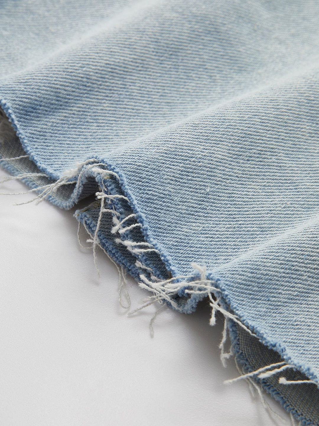 Zoom sur l'ourlet effiloché de la veste en jean courte Giselle, ajoutant un détail moderne et déstructuré. Ce design décontracté et stylé, avec un denim bleu clair de qualité, accentue l'aspect jeune et tendance de la veste, idéale pour une tenue casual chic.