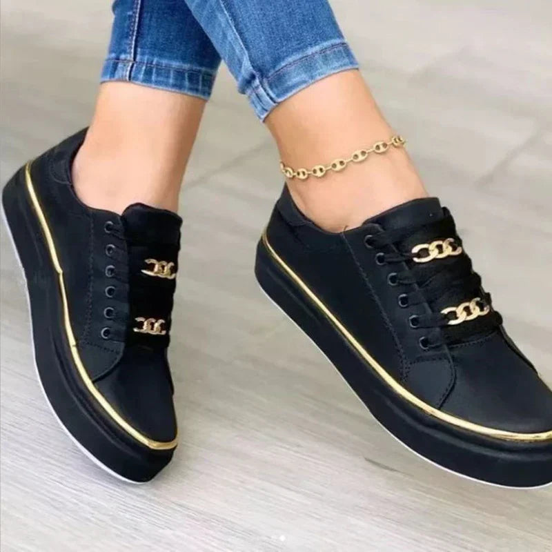 Gros plan des baskets plateforme Guenièvre noires, design moderne avec liseré doré et détails chaîne dorée sur les lacets, semelle épaisse confortable pour un style urbain élégant.