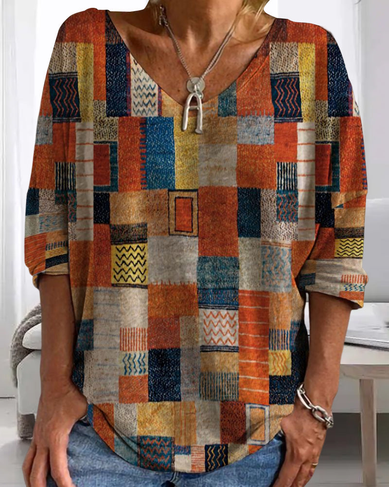 Haut d'été femme Gwladys à manches longues, style tendance col V avec imprimé géométrique aux couleurs vives (orange, bleu, jaune), porté avec un collier, sur fond intérieur.