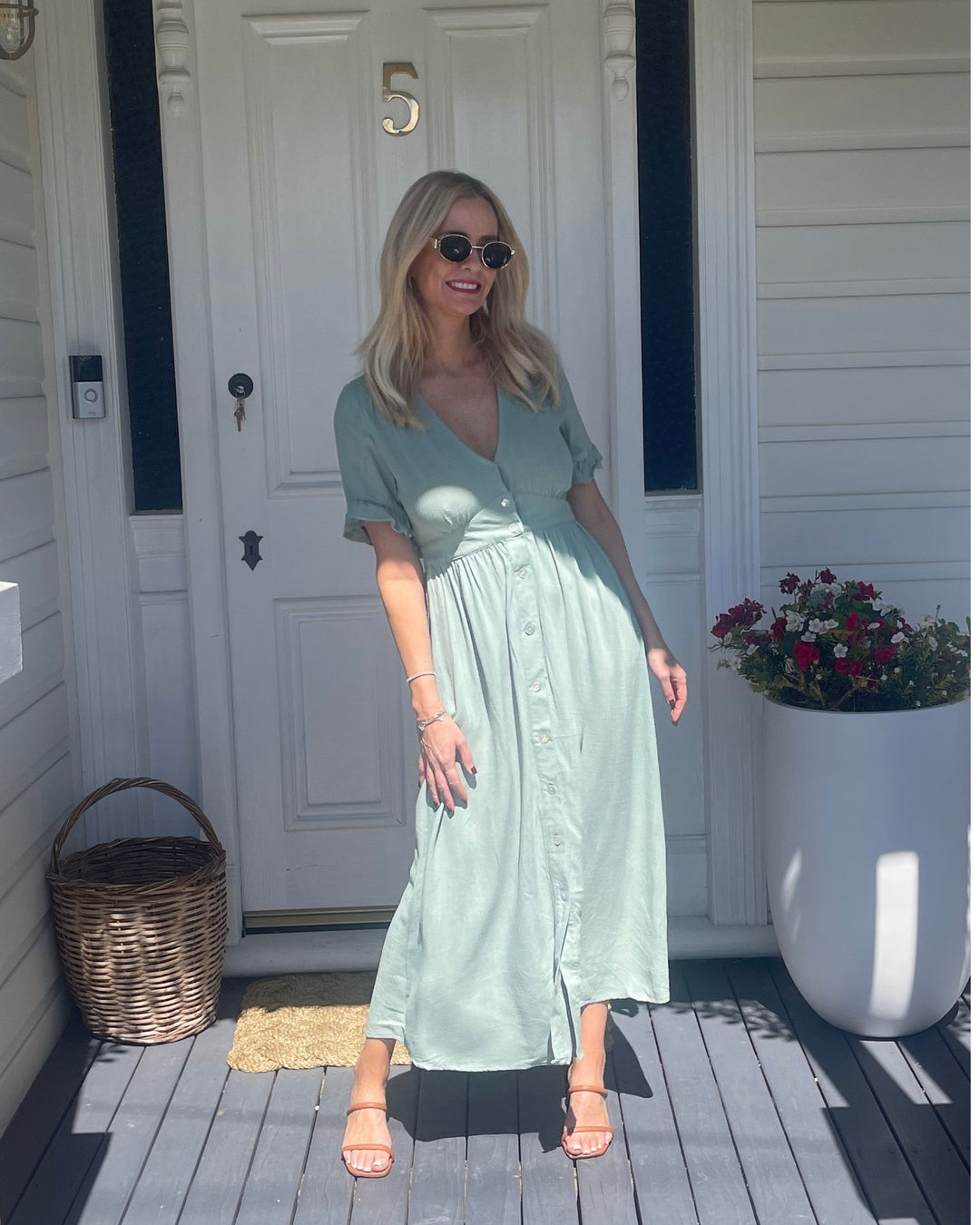 Robe midi d'été pour femme, portée par un modèle devant une porte. Le design tendance avec des manches à volants, des boutons sur le devant et une coupe fluide, parfait pour un look estival chic et décontracté.
