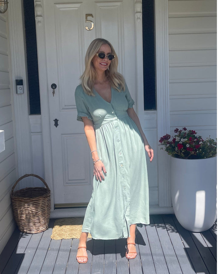 Robe midi d'été pour femme, portée par un modèle devant une porte. Le design tendance avec des manches à volants, des boutons sur le devant et une coupe fluide, parfait pour un look estival chic et décontracté.