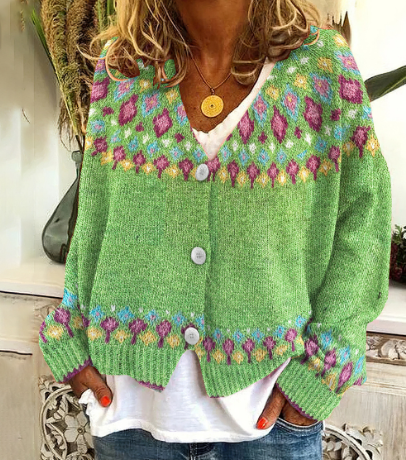 Femme portant un cardigan léger de couleur vert vif avec des motifs colorés rose, violet et bleu sur le col, les manches et le bas. Le vêtement est boutonné à l’avant et associé à un t-shirt blanc ample et un jean décontracté, créant un look estival frais et décontracté dans un intérieur lumineux.
