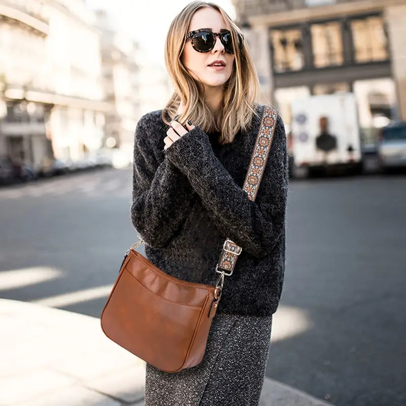 Femme portant le sac bandoulière tendance Hermine en simili cuir marron, avec large sangle réglable à motif ethnique, porté en travers du corps, en milieu urbain.