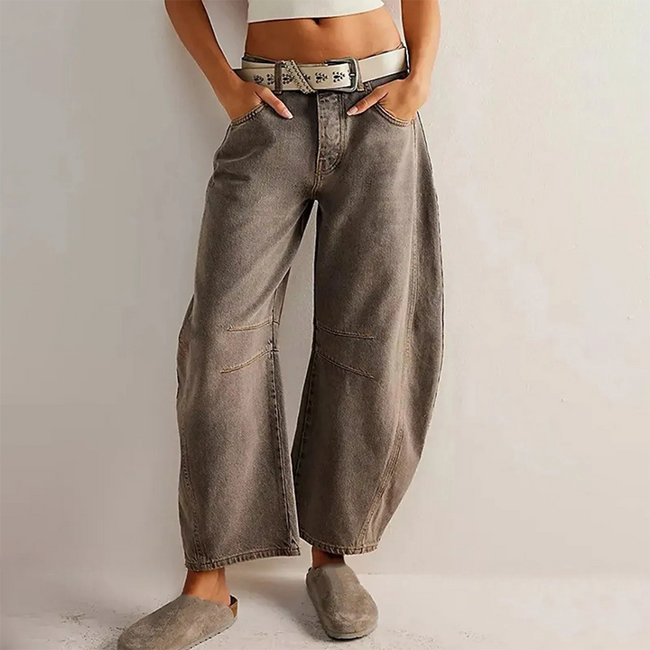 Jean large femme Hortense tendance gris taupe, coupe ample type baggy avec surpiqûres aux genoux, porté taille haute avec ceinture et crop top blanc.