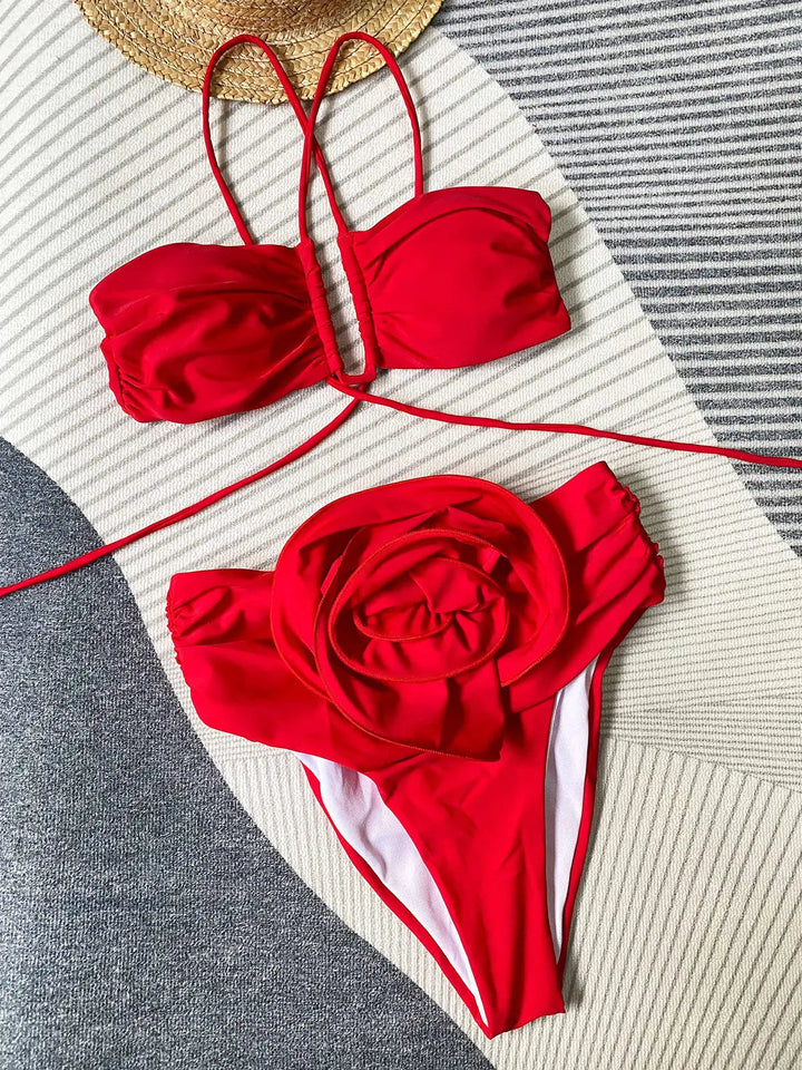 Bikini femme  rouge composé d’un haut bandeau dos nu à fines lanières et d’une culotte taille haute ornée d’une grande fleur en relief, présenté à plat pour un style tendance et élégant.