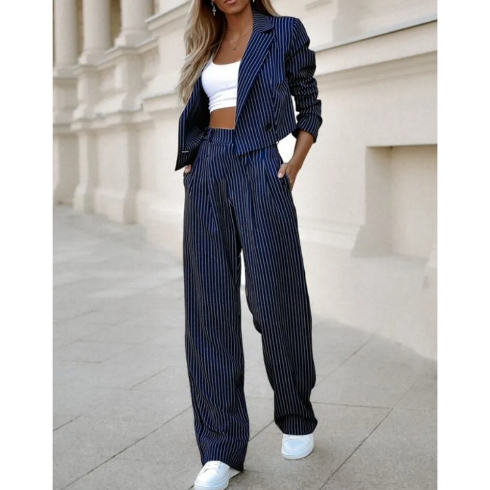 Costume formel pour femme Isabeau, moderne, bleu marine à fines rayures. Ensemble blazer cintré et pantalon taille haute à jambes larges, porté avec un top blanc et des baskets pour un look chic urbain.