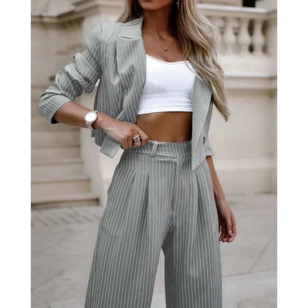 Costume formel pour femme Isabeau, moderne, gris clair à fines rayures. Ensemble blazer court et pantalon taille haute à coupe large, porté avec un top blanc pour un look chic et contemporain.