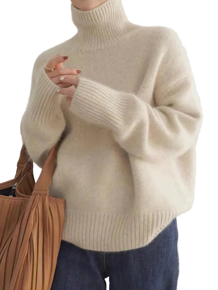 Pull d’hiver pour femme en maille épaisse de couleur beige, avec col roulé montant, coupe ample et manches longues aux poignets côtelés, porté avec un jean pour un style cosy et élégant.