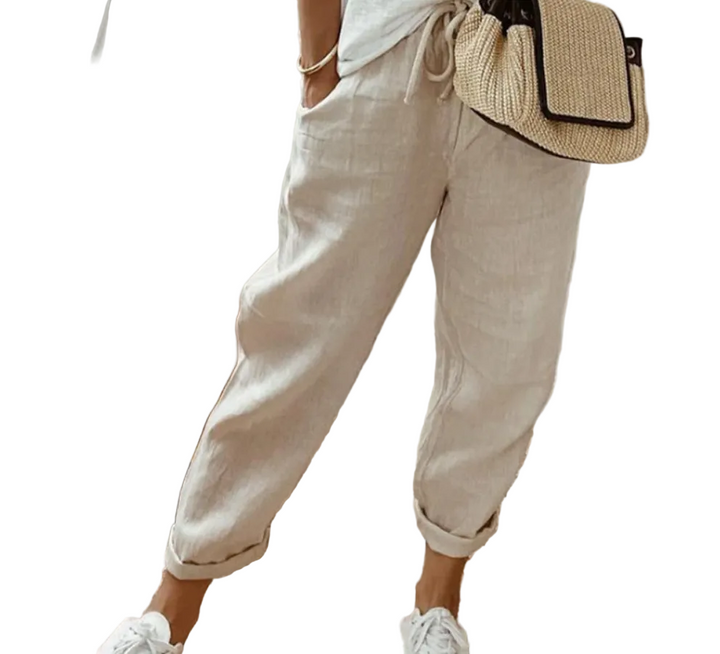 Pantalon ample pour femme en tissu léger beige clair, coupe large et confortable avec taille élastiquée et cordon de serrage, porté de façon décontractée avec des baskets blanches et un sac en paille pour un style naturel et moderne.