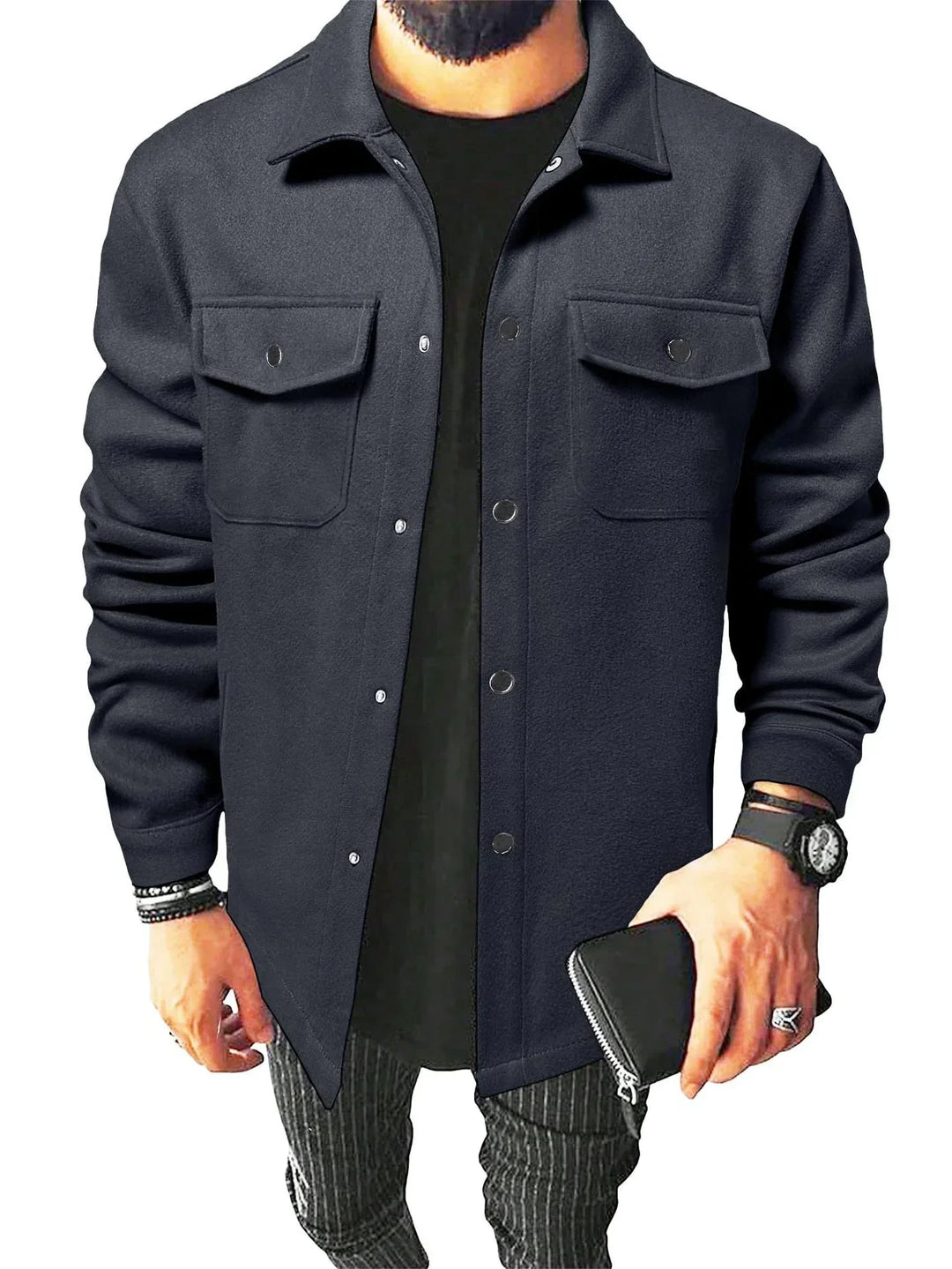 Homme portant une chemise bleu foncé avec des boutons noirs et des poches sur la poitrine, associée à un t-shirt noir en dessous. Il tient un portefeuille en cuir dans une main et porte une montre, dans un cadre moderne.