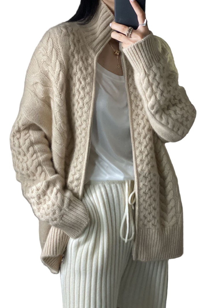 Femme portant un cardigan épais beige à col montant, en maille torsadée, ouvert sur un t-shirt blanc et assorti à un pantalon côtelé clair, pour un look confortable et tendance.