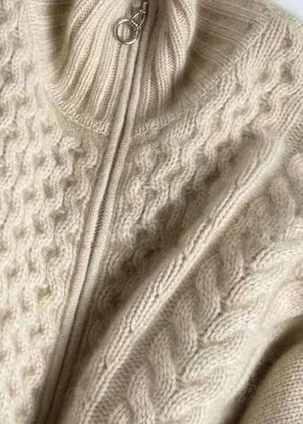 Gros plan sur un cardigan en maille torsadée beige, doté d’un col montant côtelé et d’une fermeture éclair métallique, mettant en valeur la texture douce et les détails tricotés.