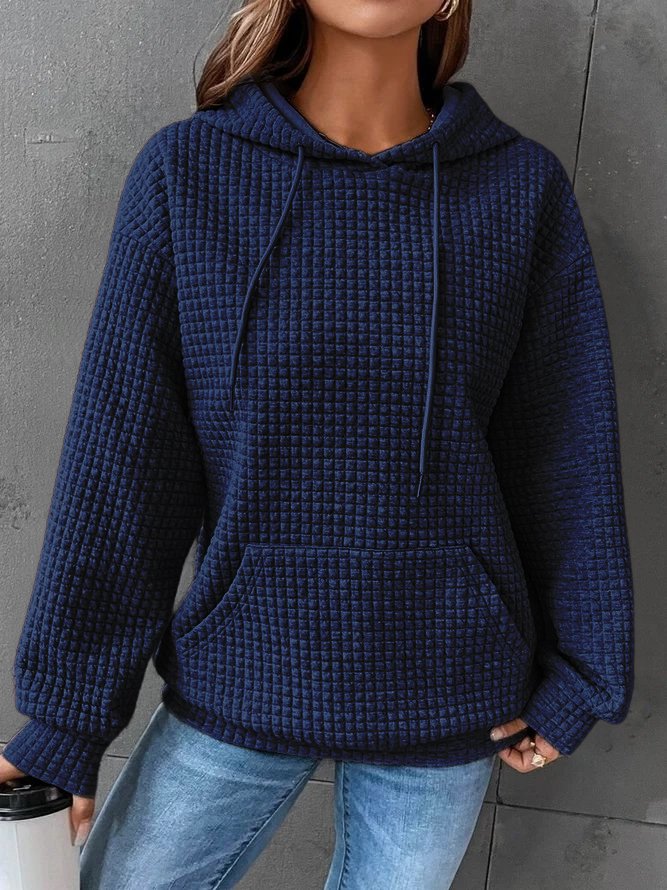 Une femme porte un sweat à capuche bleu en maille gaufrée, avec une poche avant et des cordons de serrage. Son tissu épais et doux offre chaleur et confort, idéal pour les froides journées d'hiver. Associé à un jean clair, cet ensemble dégage un style décontracté et moderne, parfait pour un look à la fois tendance et confortable.