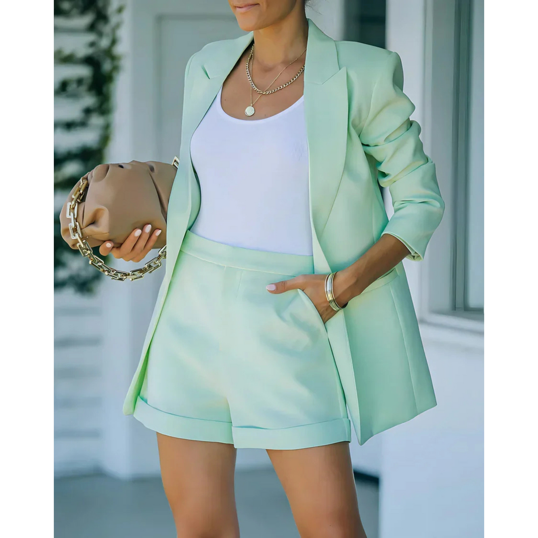 Blazer structuré pour femme de couleur vert menthe, accompagné d'un short assorti et d'un top blanc. Le look est complété par un sac à main tendance à chaîne dorée, parfait pour une tenue moderne et élégante, idéale pour les journées printanières.