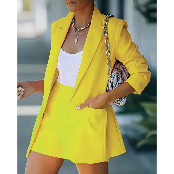Blazer structuré pour femme de couleur jaune vif, assorti d'un short et d'un top blanc. Le look est complété par un sac à main tendance, parfait pour une tenue moderne et élégante, idéale pour les journées ensoleillées.