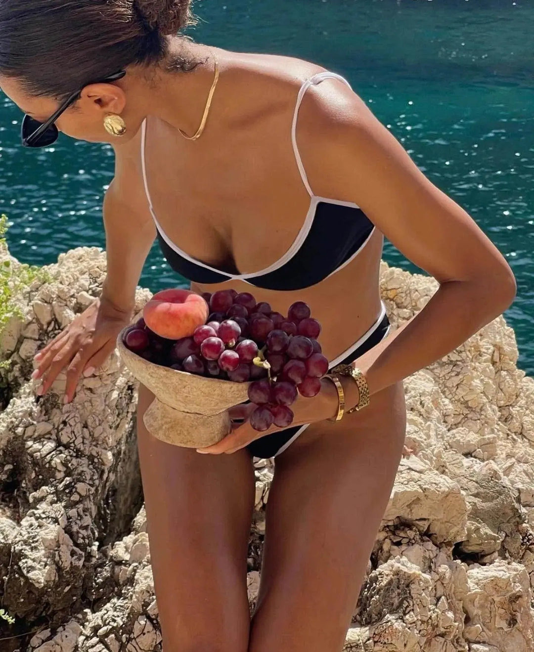 Bikini moderne pour femme Katie ensemble deux pièces noir à bordures contrastées, avec haut à fines bretelles et bas échancré, porté en bord de mer avec des accessoires élégants pour un style estival raffiné.