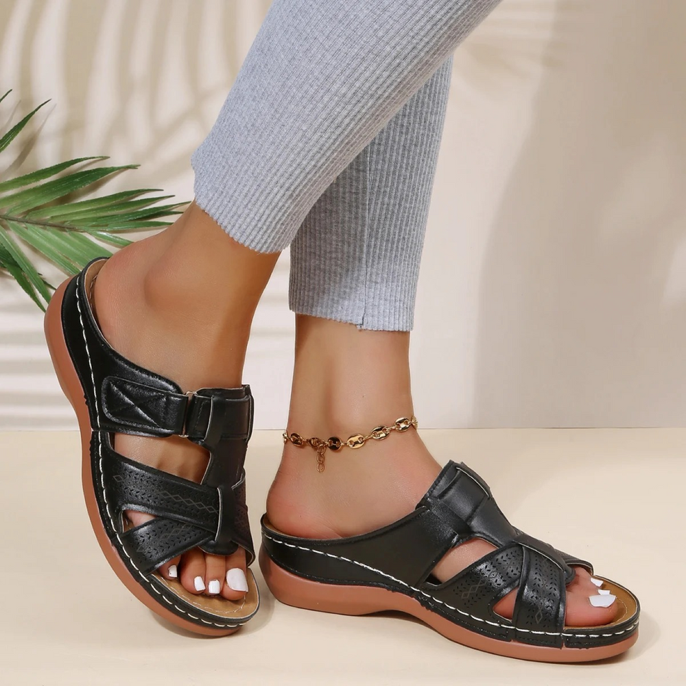 Sandales femme noires type mules avec brides ajourées et fermeture à scratch, semelle plate marron confortable, look estival décontracté.