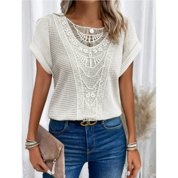 Femme portant le haut d’été Kester blanc, coupe ample à manches courtes avec détails crochet ajouré au col, style tendance et léger, associé à un jean bleu et une pochette.