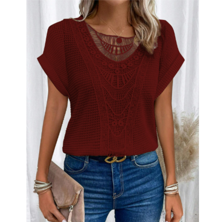 Femme portant le haut d’été Kester bordeaux, coupe ample à manches courtes avec détail crochet ajouré au col, style tendance et léger, associé à un jean bleu et une pochette.