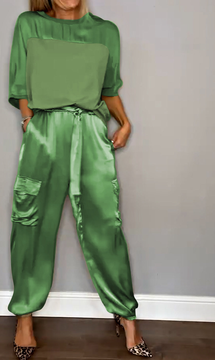Un ensemble élégant composé d'un haut satiné vert et d'un pantalon fluide avec des poches, porté avec des escarpins à motif léopard.