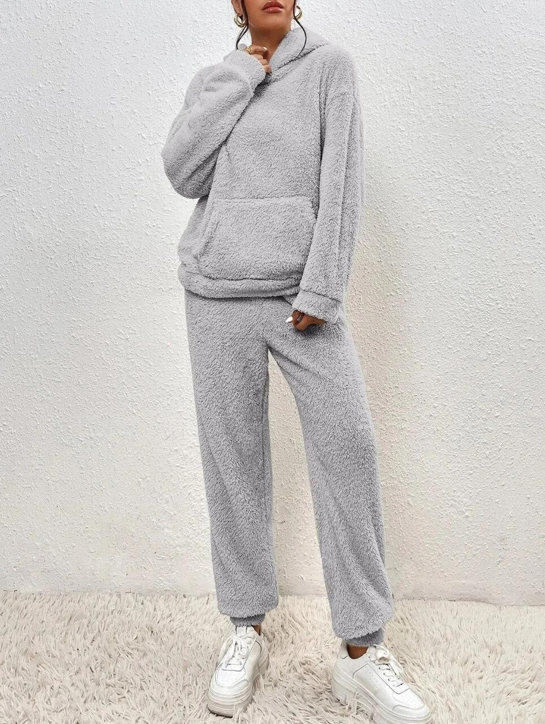Ensemble loungewear en tissu teddy gris clair pour femme, composé d’un hoodie doux à poche frontale et d’un pantalon ample assorti, offrant un style confortable et moderne pour les moments de détente.
