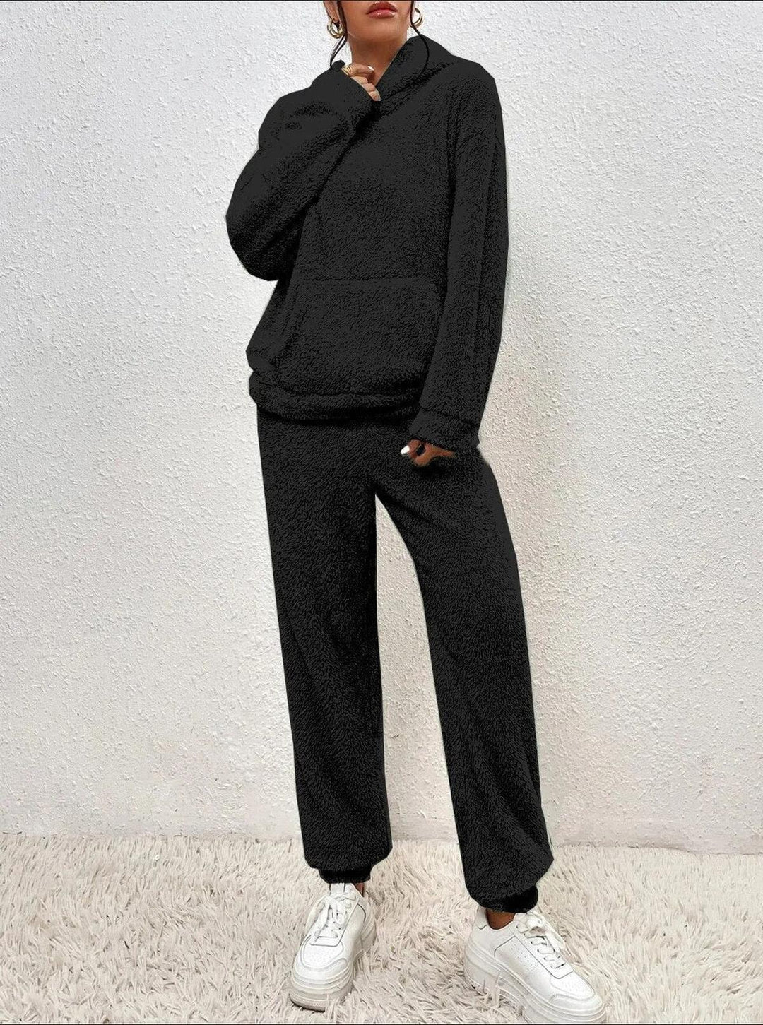 Ensemble loungewear noir en tissu teddy pour femme, composé d’un hoodie ample et d’un pantalon confortable, présenté en pleine hauteur sur un tapis doux, mettant en valeur son look cosy et moderne.