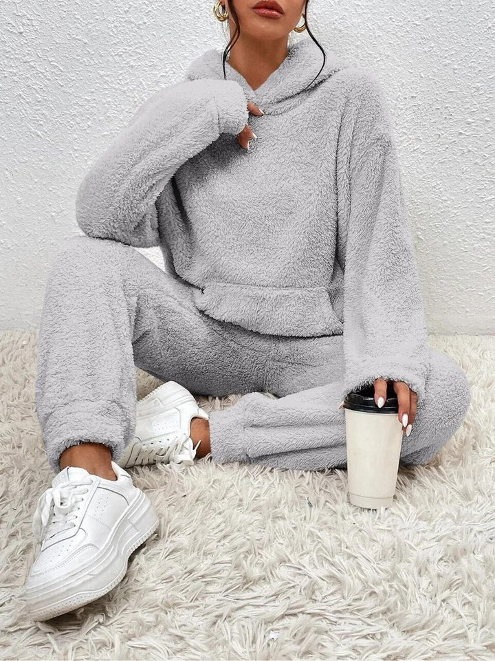 Ensemble loungewear en tissu teddy gris clair pour femme, avec un hoodie doux et un pantalon confortable, présenté sur un fauteuil pour mettre en avant son style cosy et moderne.