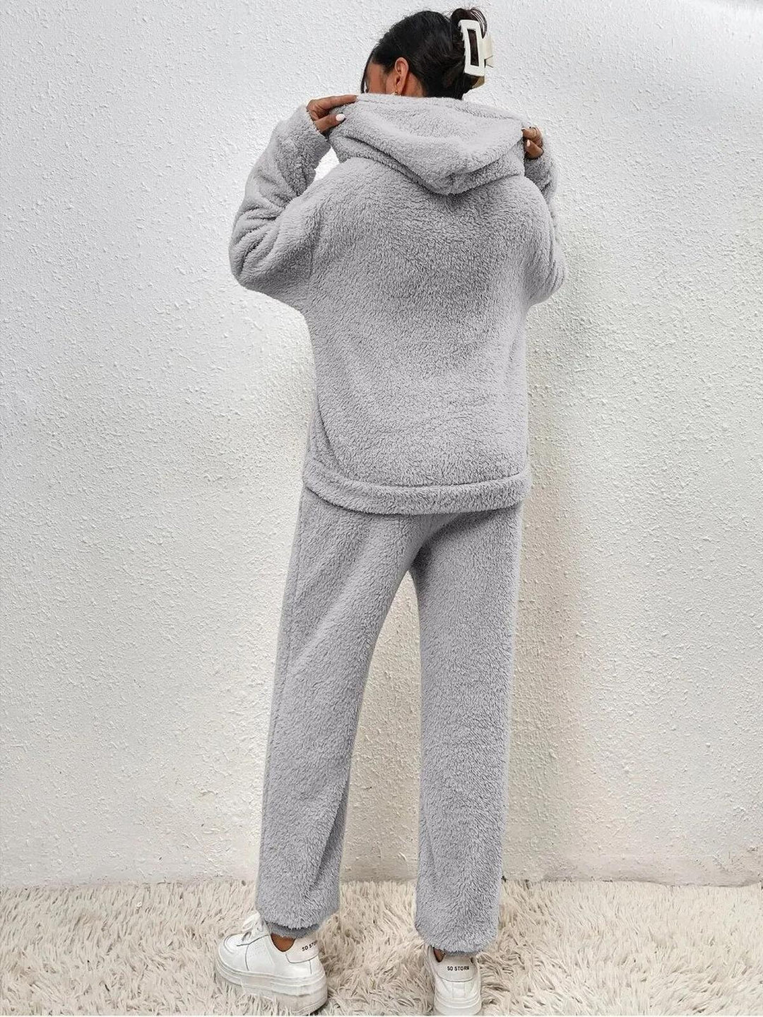 Ensemble loungewear doux en tissu teddy gris clair pour femme, montré de dos avec un hoodie confortable et un pantalon ample, mettant en avant sa texture moelleuse et son style cosy.