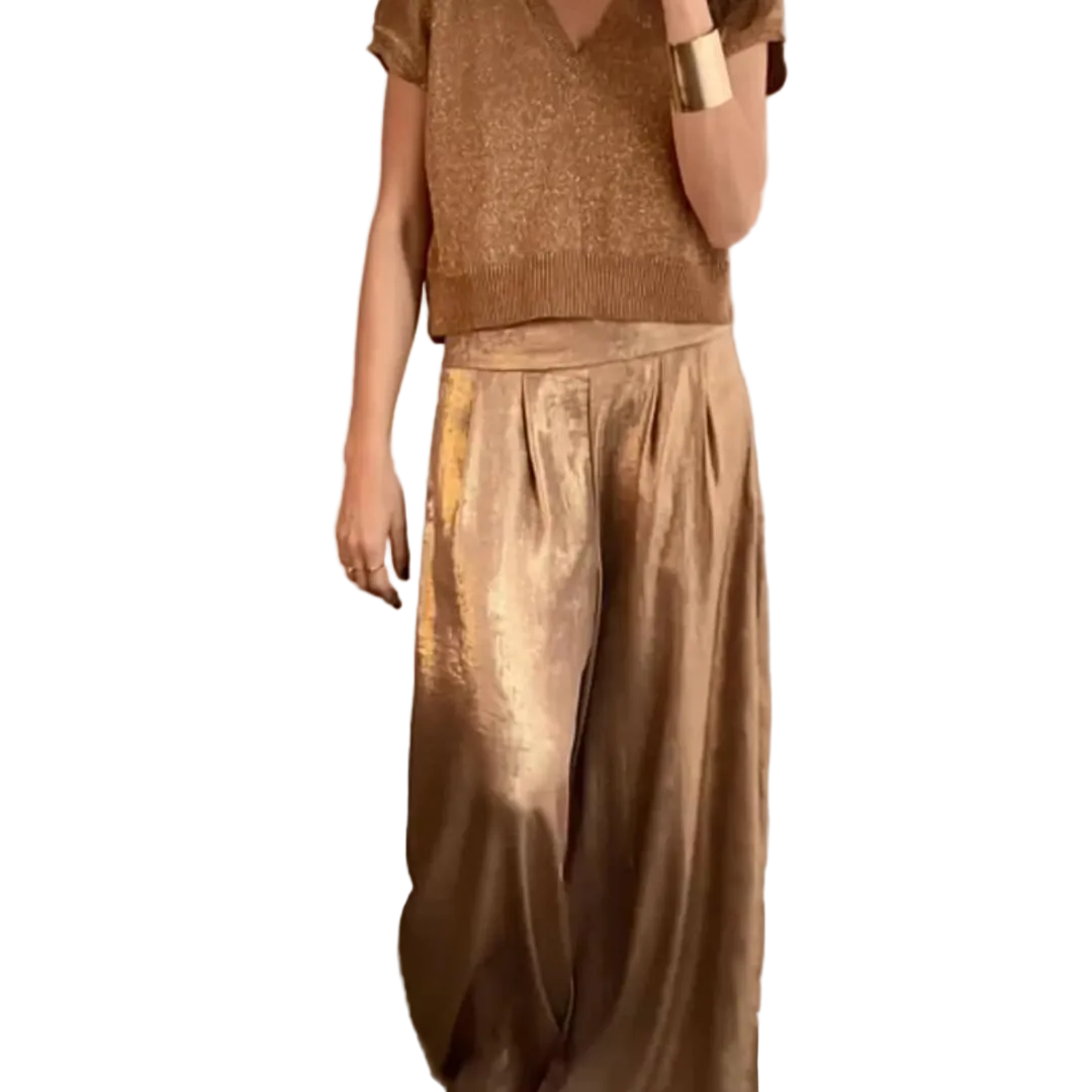 Femme portant un ensemble élégant composé d’un haut à manches courtes et d’un pantalon large taille haute, de couleur beige doré à l’aspect satiné, dans un intérieur raffiné au style chic et moderne.