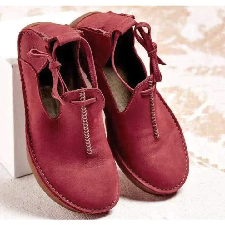 Chaussures d’automne pour femme en cuir suédé bordeaux, avec bout arrondi, coutures apparentes et lien décoratif sur le côté, présentées sur un fond clair pour un style moderne et chaleureux.