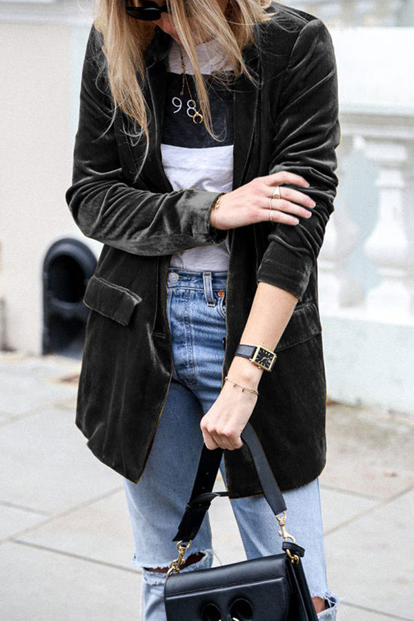 Une femme portant une veste en velours noire avec des manches retroussées, une chemise à rayures et un jean décontracté. Elle porte un sac à main noir et une montre, affichant un look élégant et décontracté.