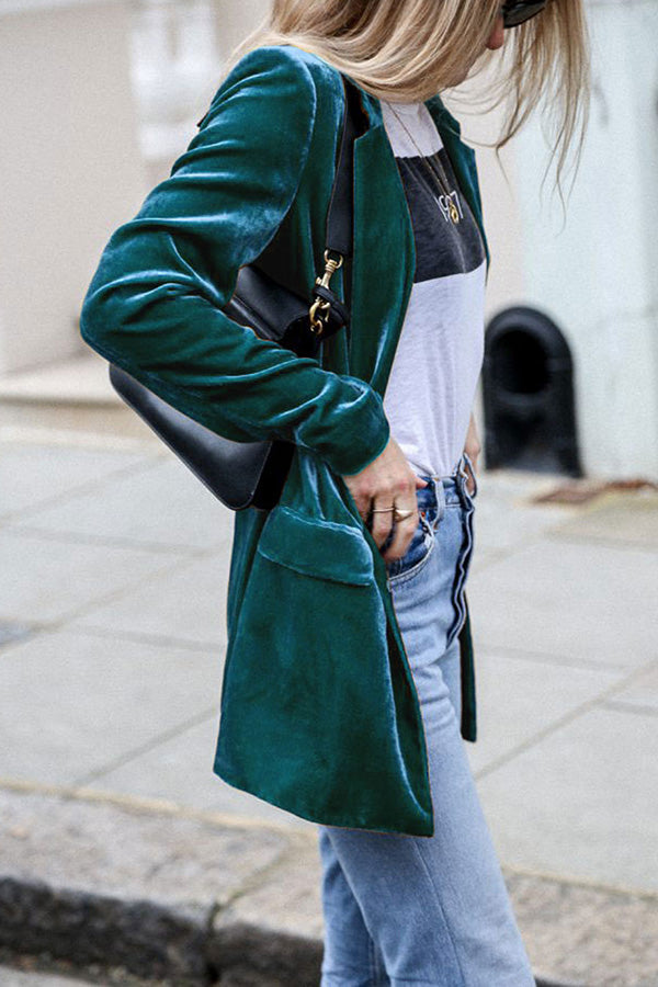 Une femme portant une veste en velours verte avec des manches retroussées, une chemise blanche à rayures et un jean bleu clair. Elle porte un petit sac à main noir, affichant un look élégant et moderne.