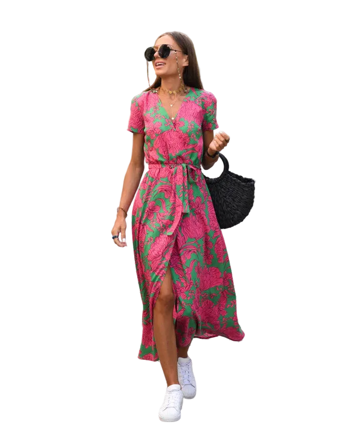 Robe midi Layla pour femme, col en V et coupe moderne, imprimé floral rose sur fond vert, taille ceinturée et manches courtes, portée avec des baskets blanches et un sac noir pour un style chic et décontracté en ville.