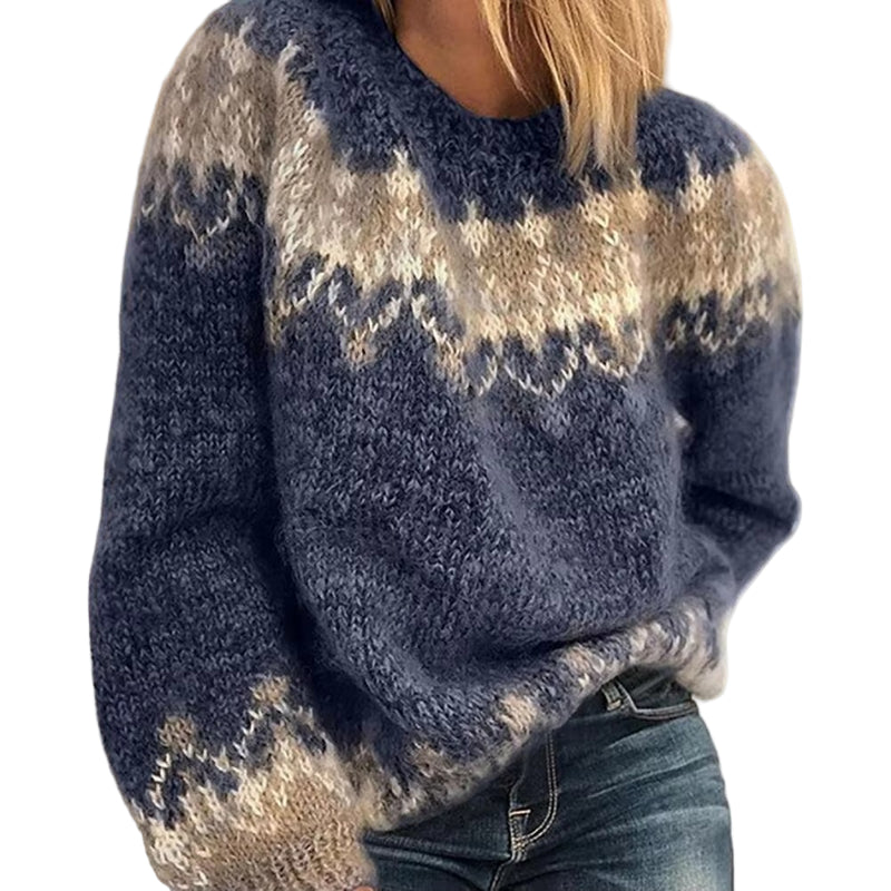 Une femme porte un épais pull d'hiver en laine douce, bleu avec des motifs nordiques beiges et crème sur le haut. Ce vêtement ample et confortable est idéal pour une allure à la fois chaleureuse et élégante durant la saison froide.