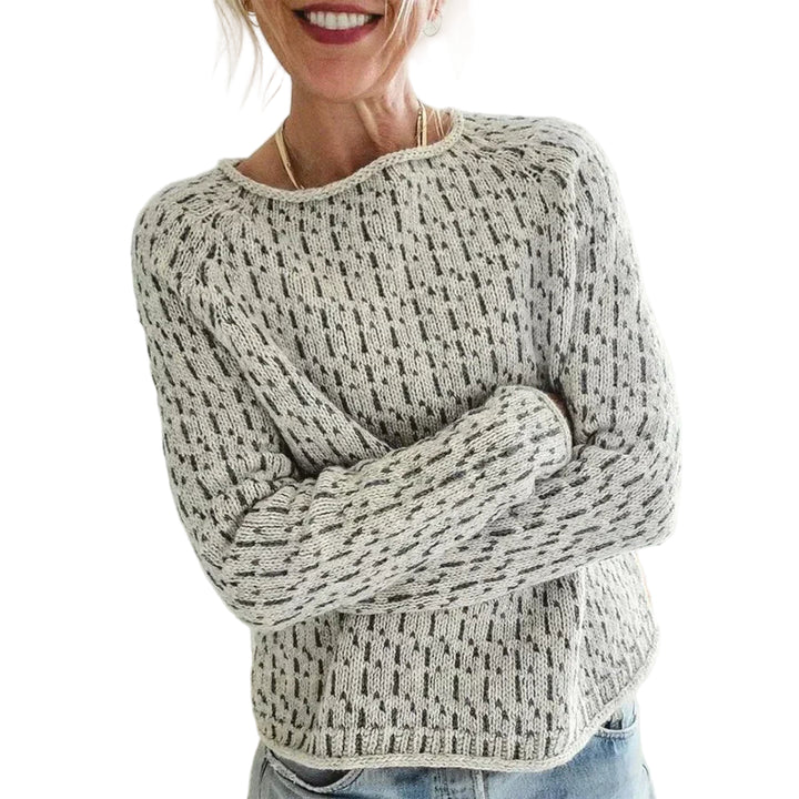 Femme souriante portant un pull en maille clair à col rond, avec un motif texturé discret et une coupe décontractée, posant dans une pièce lumineuse.