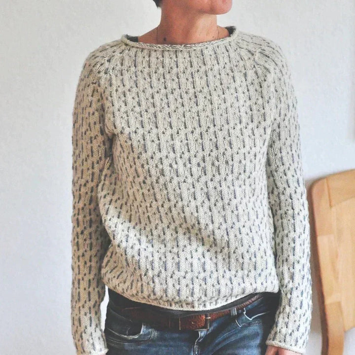 Femme portant un pull en maille clair à col rond, doté d’un motif texturé discret et d’une coupe décontractée, associé à un jean dans un intérieur simple et lumineux.