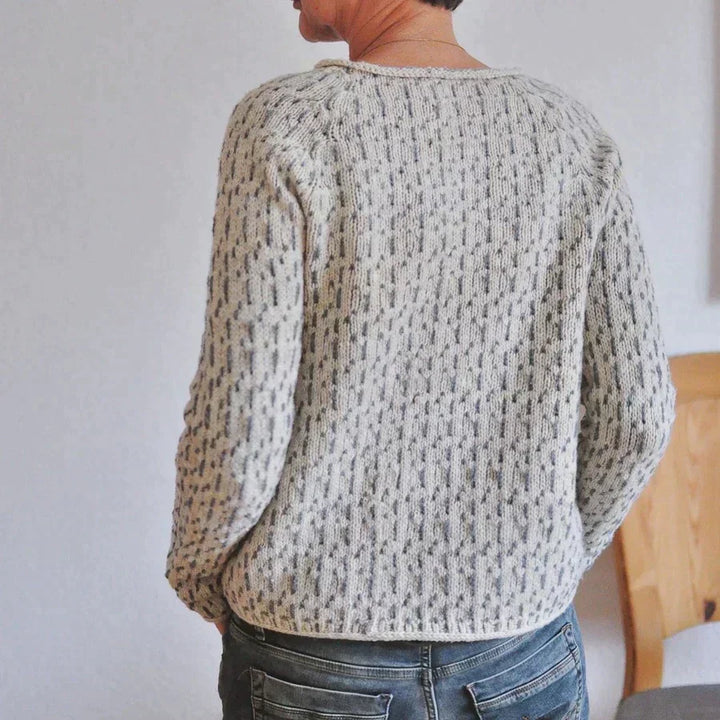 Vue de dos d’une femme portant un pull en maille clair à col rond, avec un motif texturé discret et une coupe décontractée, associée à un jean dans un intérieur lumineux.