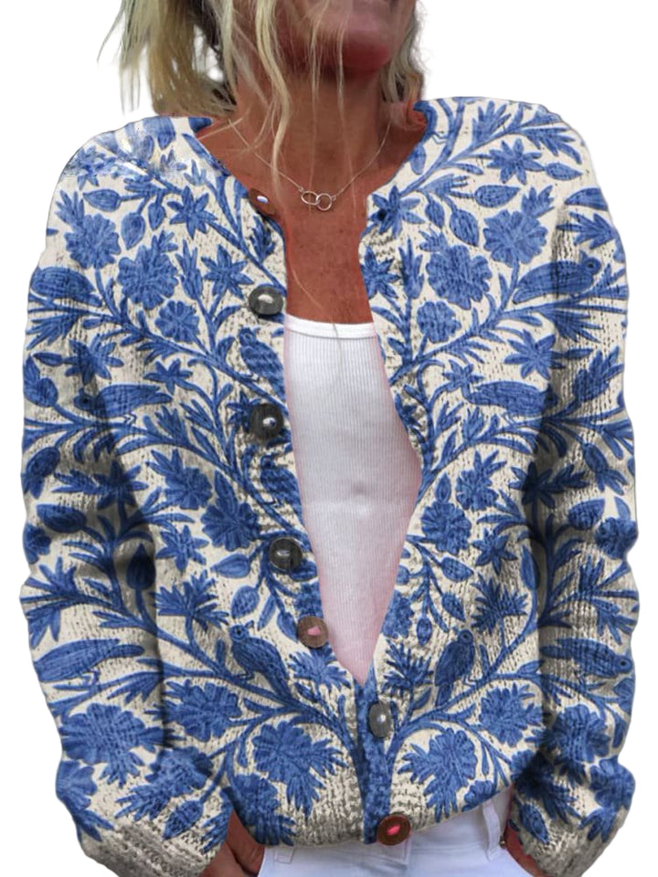 Femme portant un cardigan en maille clair décoré de broderies florales bleues, avec une coupe moderne et des boutons sur le devant, posant en extérieur.