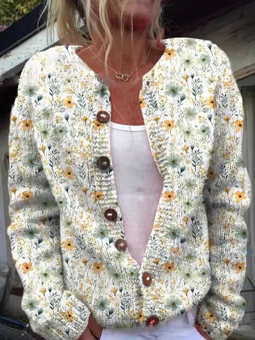Femme posant en extérieur, vêtue d'un cardigan blanc en maille légère orné de broderies florales jaunes et vertes, avec des boutons en bois et une coupe moderne.