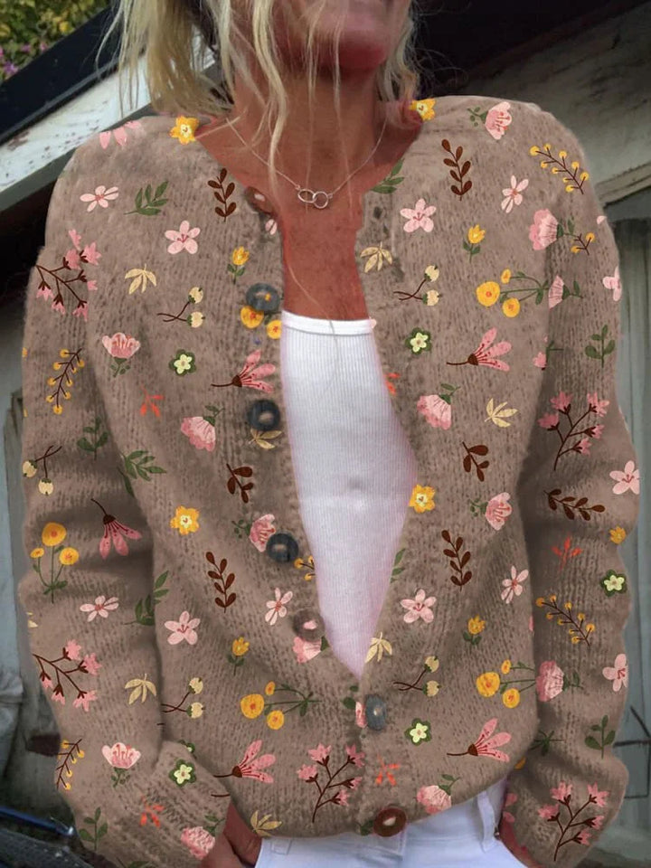 Femme portant un cardigan en maille marron orné de broderies florales roses, jaunes et marron, à la coupe moderne et boutonné sur le devant, posant en extérieur.