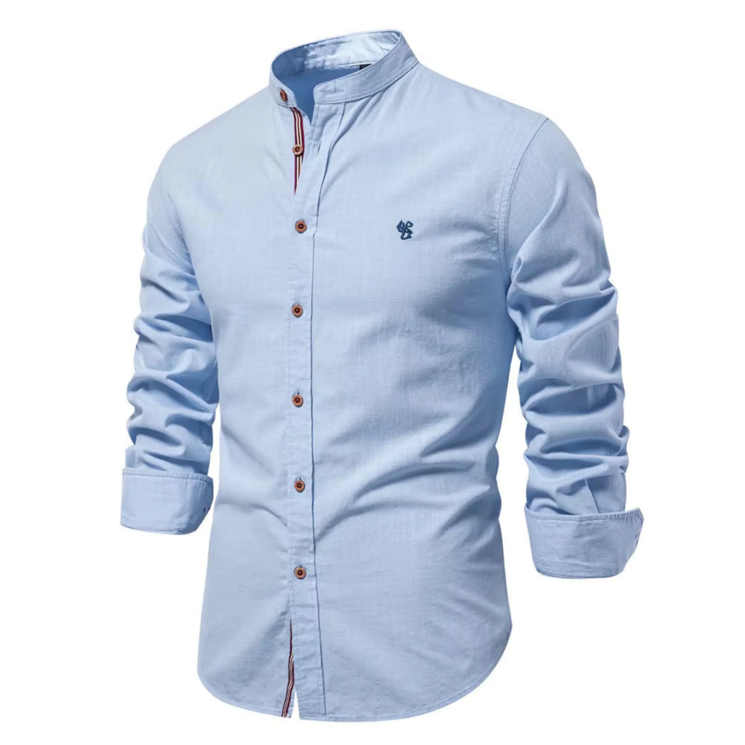 Cette chemise à manches longues de couleur bleu clair présente un col Mao et des boutons en bois contrastés. Elle est décorée d'un petit logo brodé sur la poitrine, offrant une allure élégante et décontractée, idéale pour les journées fraîches.